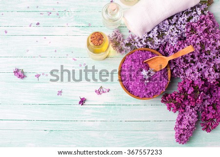 Spa setting. Natural sea salt, organic aroma oils, lilac flowers, towels on turquoise painted wooden planks. Selective focus. Place for text. Top view.