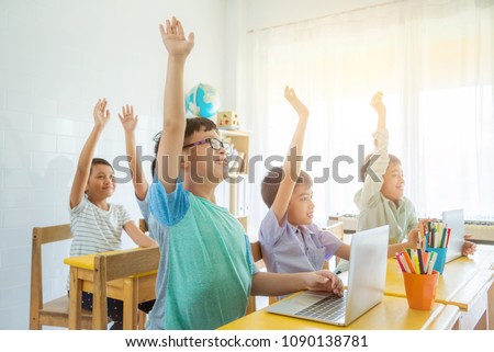 Asian school children rising hand up with smile in classroom