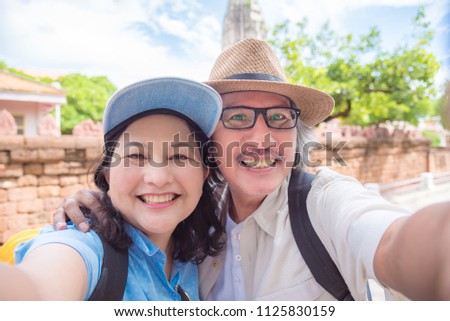 Happy asian retired couple taking their photo by smart phone at a temple in Thailand