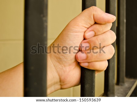 Hand of the prisoner on a jail bar