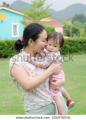 Asian mom nuzzles her daughter cheek in garden