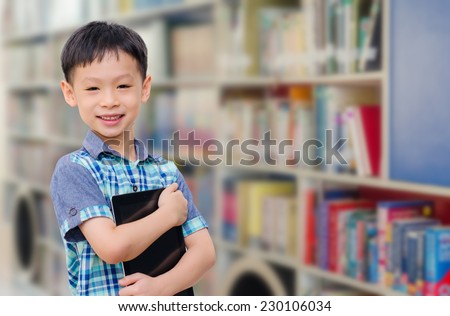 Asian boy with tablet computer in school library smiling at came