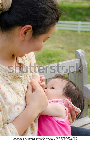 Asian mom breast feeding her baby girl in park