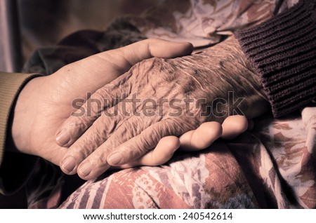 Young girl\'s hand touches and holds an old woman\'s wrinkled hand