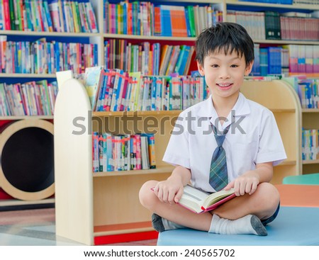 Asian boy student in uniform reading book in school library