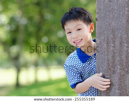 Portrait of little Asian boy peeking from behind tree with blur