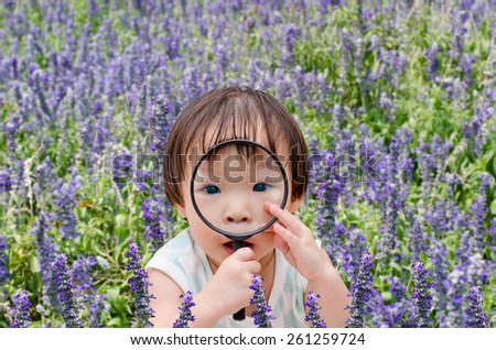 Little Asian girl with magnifying glass in flower field