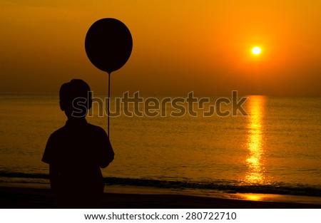 Lonely boy  holding balloon and looking sunset on the beach  while waiting for his parent come home