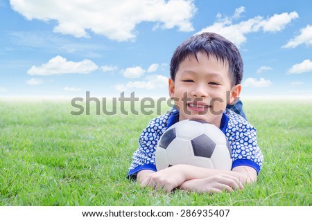 Little Asian boy smiles with his football on field