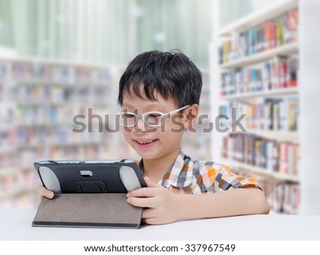 Asian boy student searching information by tablet computer in school library
