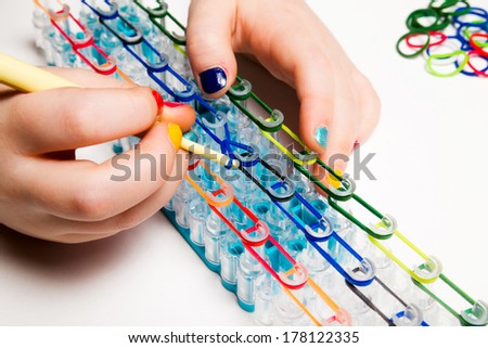 Little girl with colorful nails making a rubber loom bracelet with a hook . Hands close up. Young fashion concept