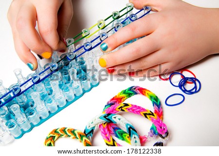 Little girl with colorful nails making a rubber loom bracelet with a hook . Hands close up. Young fashion concept