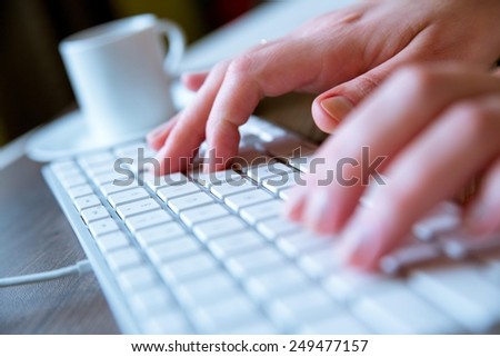 Young woman typing on a white modern computer keyboard while having a coffee on the side.