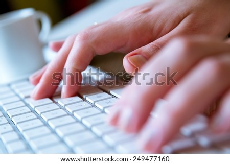 Young woman typing on a white modern computer keyboard while having a coffee on the side. Soft focus detail. Modern, business,finance, computer, technology, hacking and job hunting concept. High key.