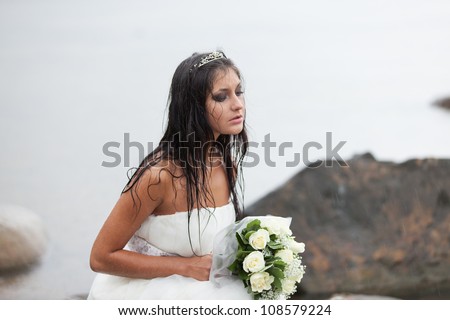 Sad bride sitting on the sea-shore and crying in the rain