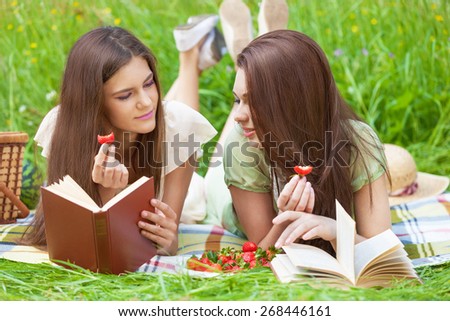 Two beautiful girls on picnic eating strawberry while reading books