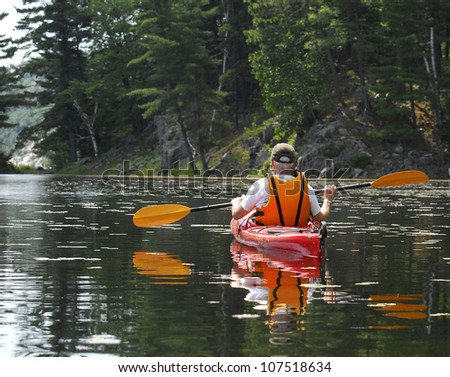 A male glides a kayak through quiet water on a peaceful wilderness lake.