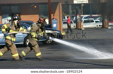 Fireman with hose extinguishing a car fire.