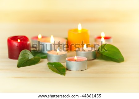colorful burn scented candles  with green leaves  on wood background