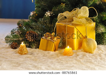 golden Christmas gift boxes with burn candles under decorated fir on snow
