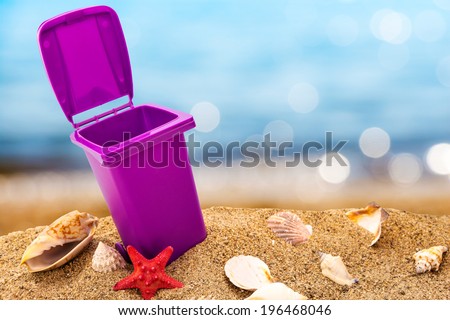 Trash can on clean sand and shells with seascape background