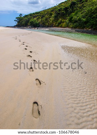 footprints on Sandy Bay beach in New Zealand. Incredible orange sand and turquoise water