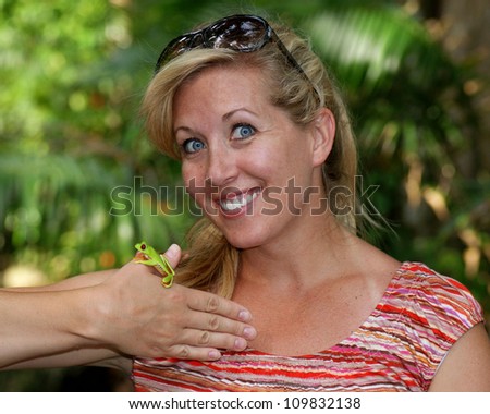 Woman smiling and holding a colorful frog in a tropical setting - the Red-Eyed Tree Frog, Agalychnis callidryas