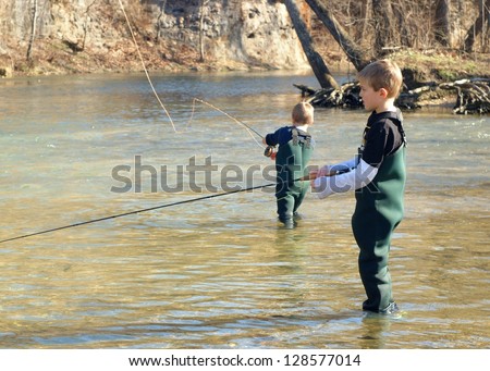 Children fishing - brothers and friends learning to fly fish in a clear stream (focus centered on boy in front)