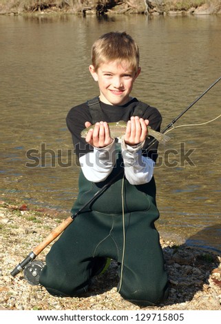 Children fishing -- boy fly fishing, holding his prize catch (a rainbow trout) and fly rod