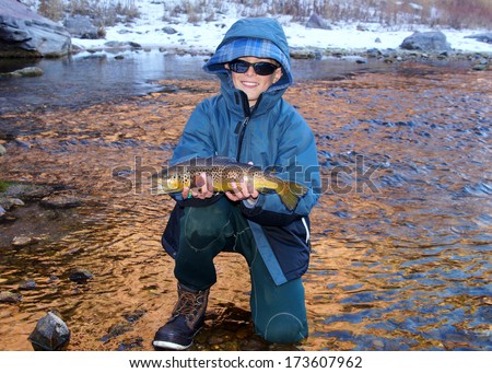 Boy fishing - young boy in a coat and sunglasses poses with a large fish he caught fly fishing in the winter (Brown Trout)