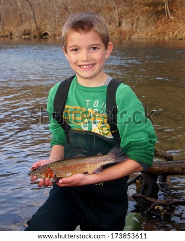 Boy fishing - Smiling youth in waders holding a Rainbow Trout fish next to a clear stream