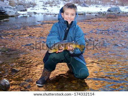 Boy fishing - young man with a nice fish (Brown Trout) caught fly fishing in a river on a cold winter day