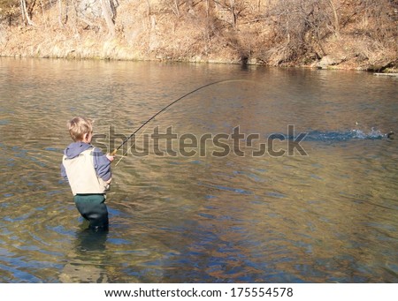 Boy fly fishing - a boy fighting a big fish with his fly rod or pole, fish jumping and splashing at end of line