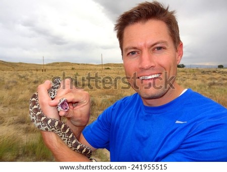 Man carefully holding a biting snake - Pituophis catenifer sayi