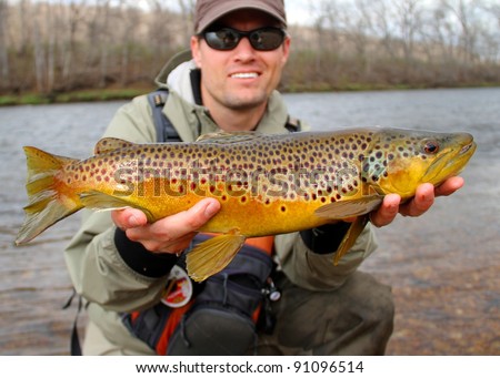 Fly fisherman holding a huge Brown Trout fish prior to releasing into the river