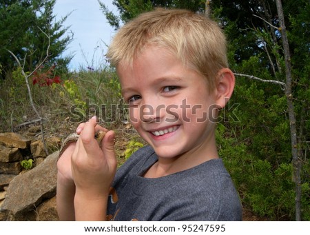 Kids catching animals - boy holds a large lizard reptile caught playing outdoors
