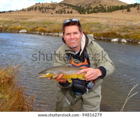 Handsome man outdoors in nature - holding a brown trout fish caught fly fishing in a mountain stream