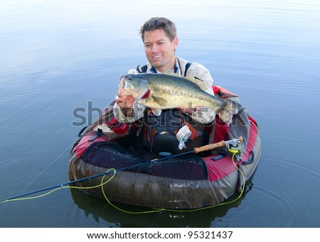 Fly fisherman in pontoon, float tube or belly boat, with large Largemouth Bass caught fishing with fly rod