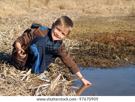 A child playing outside and learning about nature while getting messy in a wetland pond, with tadpoles in hand