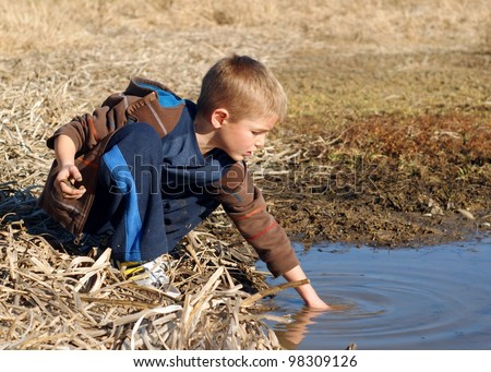 Young boy playing in water of a wetland pond - getting dirty catching frogs and fish