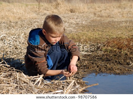 Young boy playing and getting muddy in a wetland pond - learning about nature by catching tadpoles, fish, shrimp and aquatic insects