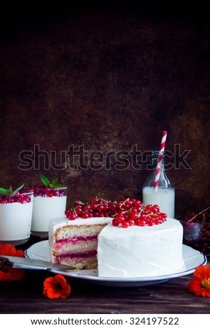 Cakes with red currant decorated with fresh red berries and flowers, cream desserts with berries, milk and old books on dark wooden background
