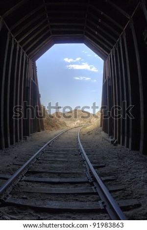 Light at the end of the tunnel. View inside a railroad tunnel - daylight, clouds, and mountains outside the opening.
