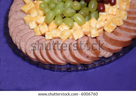 A meat tray with cheese and grapes.