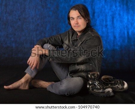 Young casual man sitting on the floor while barefoot, in studio