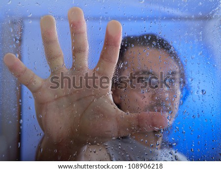 young adult man looking through the window on a rainy day. focus on the raindrops on the glass