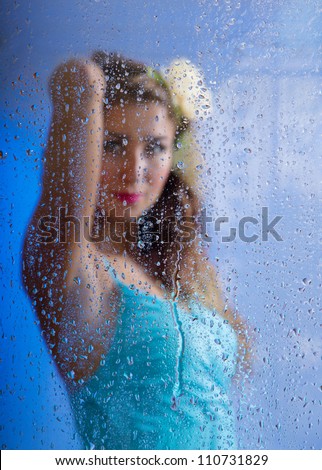 Young beautiful girl looking through window after rain. Focus on rain drops.
