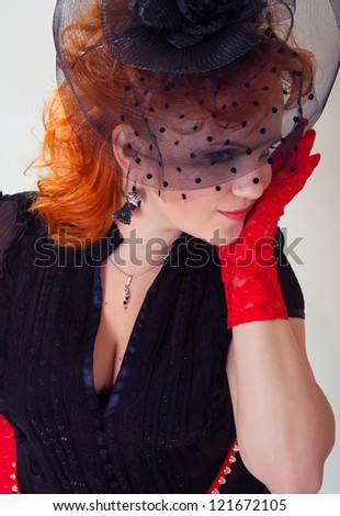 Portrait of a young woman with red hair in black hat with net veil and red gloves in retro style