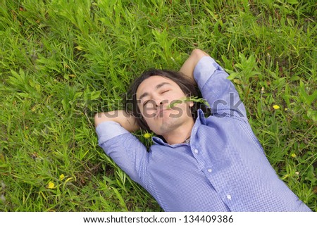 Close up of young handsome business man relaxing outdoor lying on back on green grass