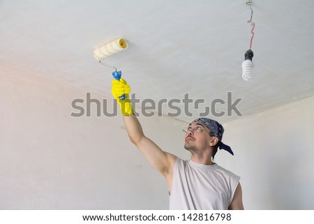 Young worker painting ceiling with painting roller